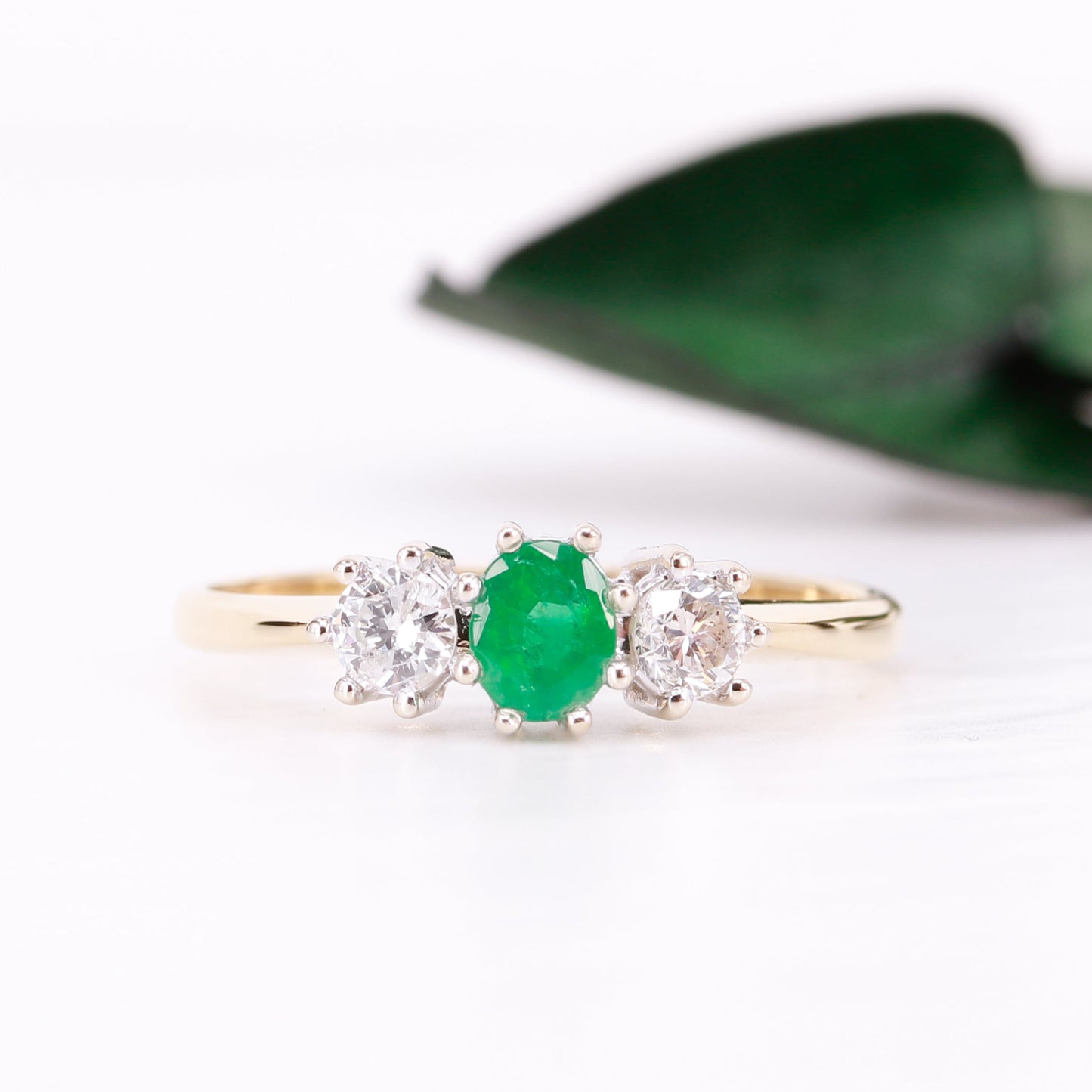 Gold ring with a green gemstone and two diamonds on a white background