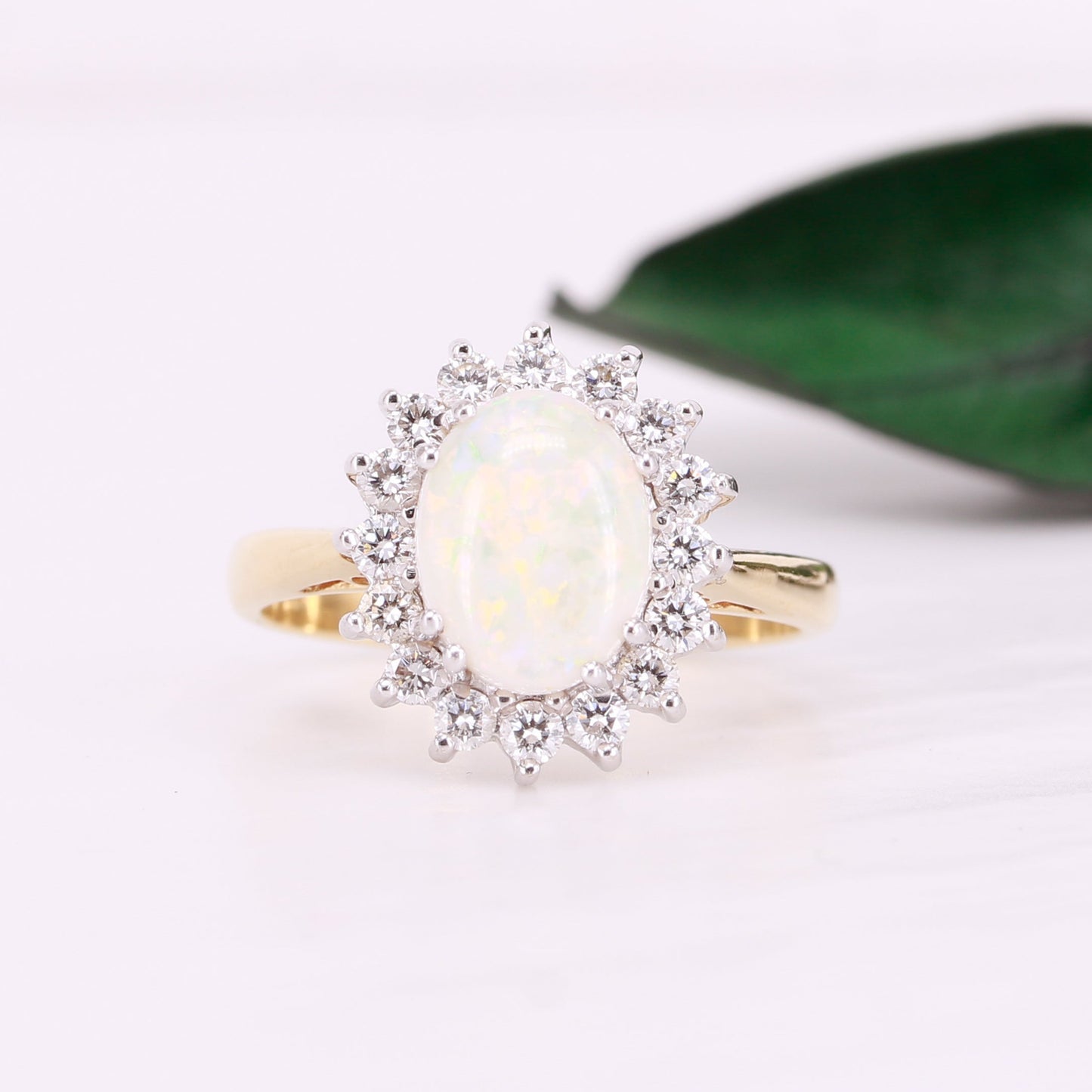 Gold ring with a large oval cut opal central gemstone and a diamond halo surround on a light background