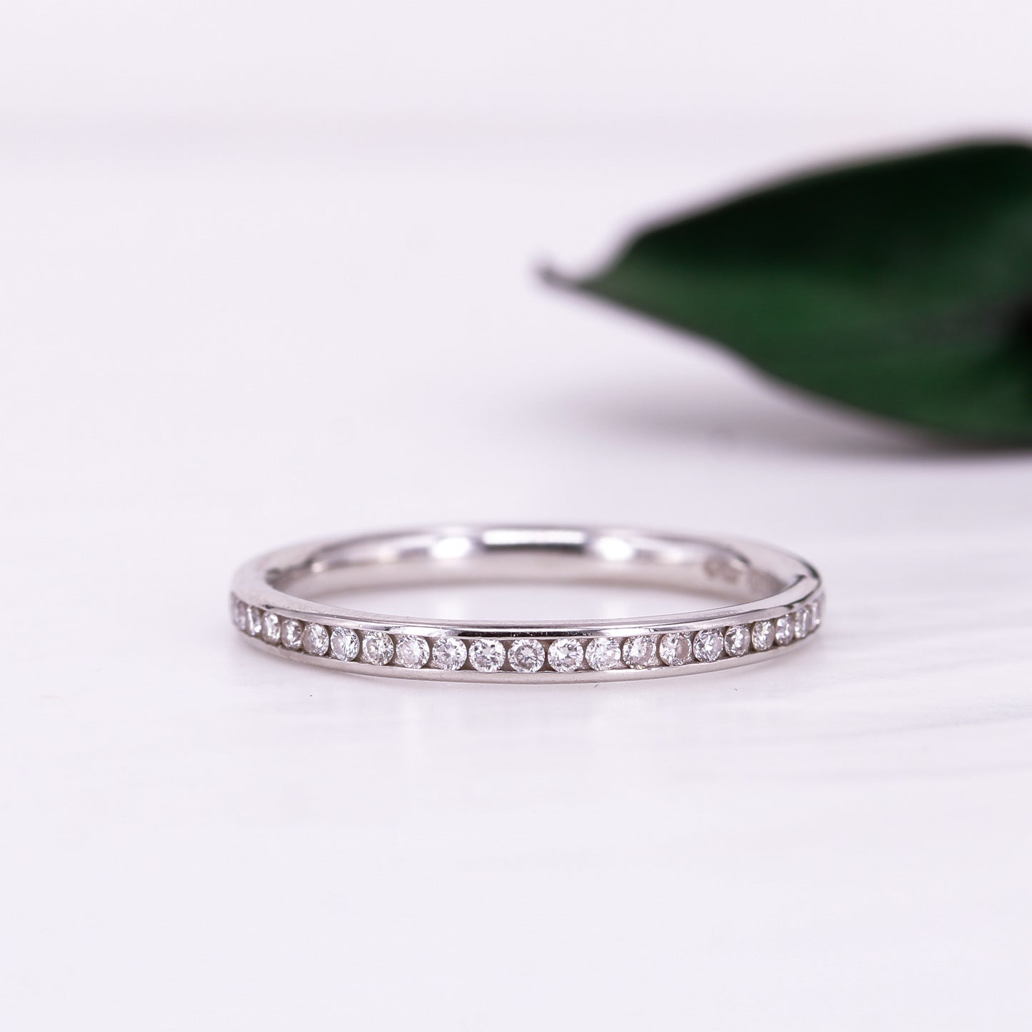 Platinum ring with small diamonds channel set on a white background with a green leaf.